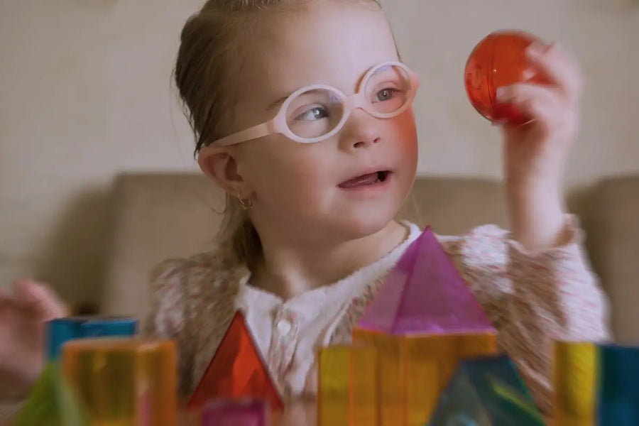 Bambina con disabilità intellettiva che osserva con curiosità una sfera trasparente, circondata da forme geometriche in plastica colorata