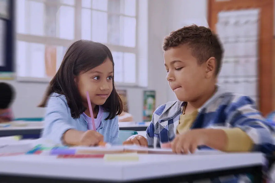 bambina e bambino su un banco di scuola che imparano a scrivere